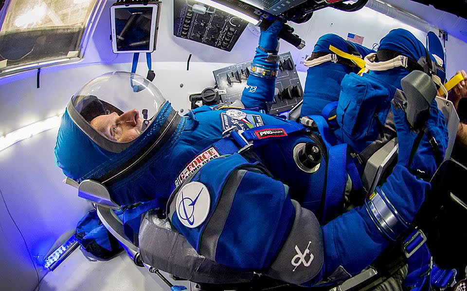 Astronaut in spacesuit within a Starliner space capsule.