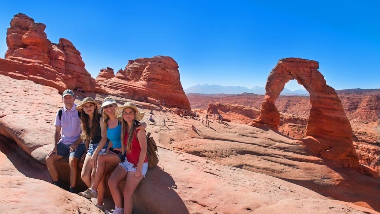 Smiling happy family on vacation hiking trip. People relaxing on top of mountain next to Delicate Arch enjoying time together. Arches National Park, Utah, USA
