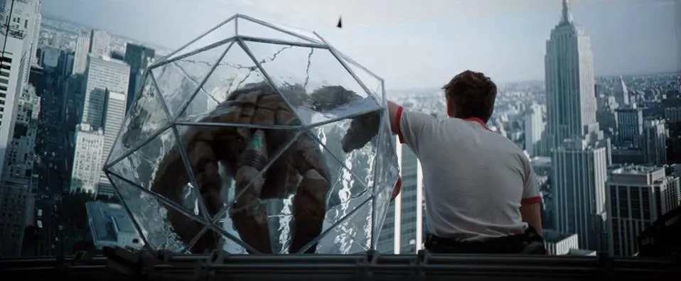 An alien in a clear ball sitting next to a man wearing a white T-shirt