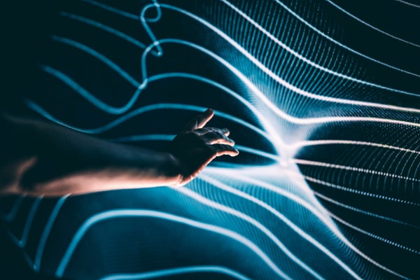 A human hand outstretched towards a rippling, light-dappled surface of abstract interwoven lines