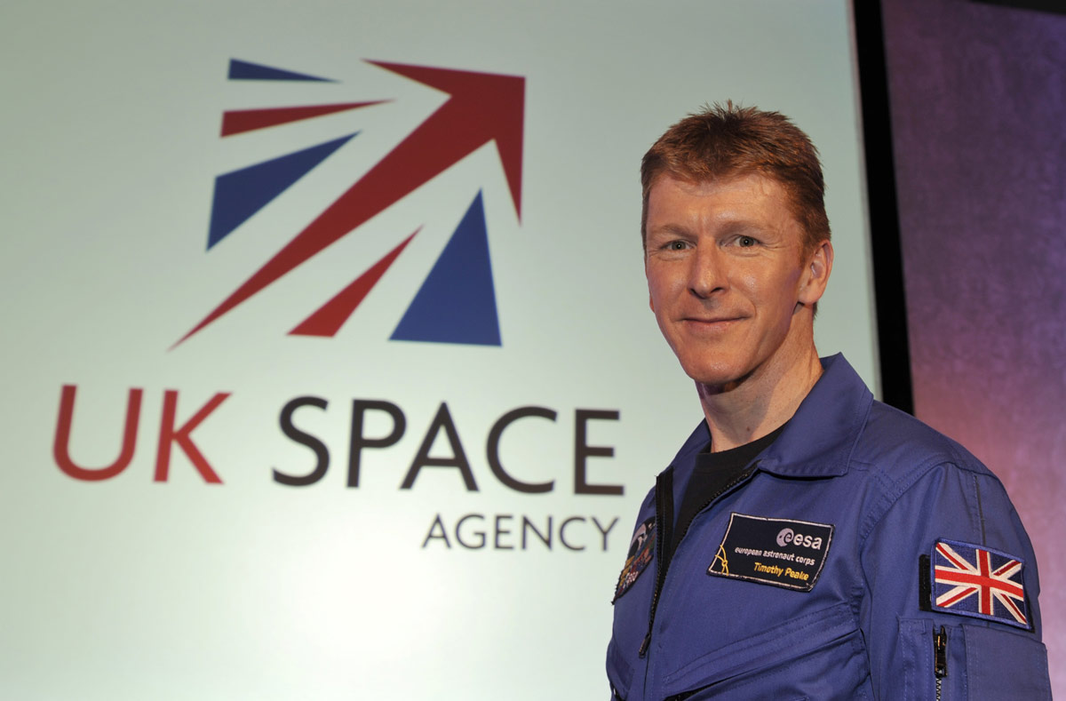 A man wearing a blue jumpsuit with the UK flag stands in front of a sign reading "UK Space"