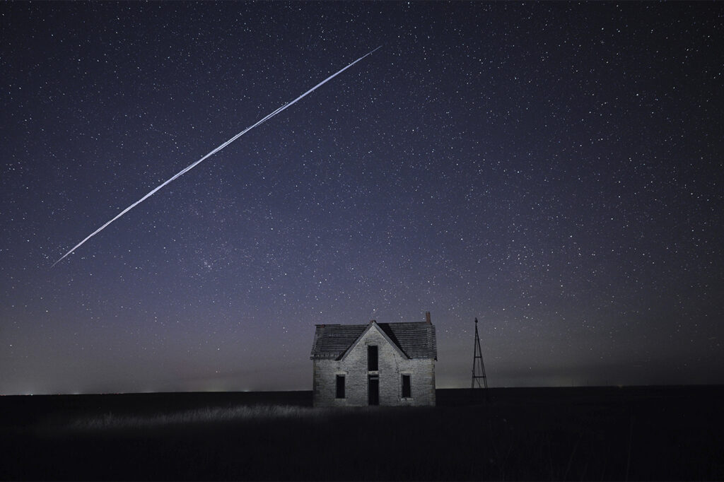 A long exposure view of StarLink satellites traveling across the night sky above a lone house.