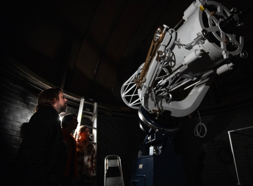 Visitors stand beneath the dome looking up at the observatory’s large white telescope during the Star Party.