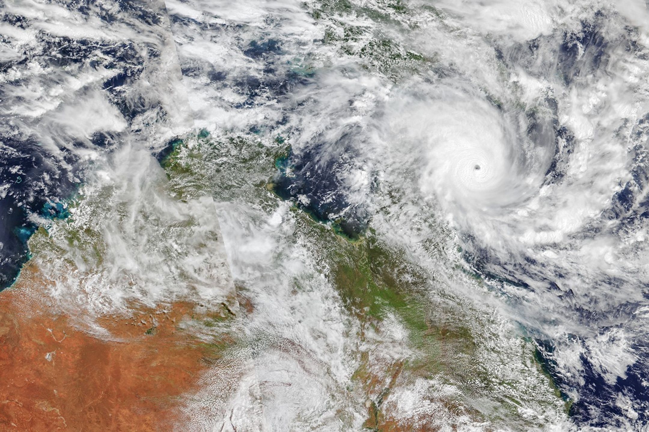 A tropical cyclone with spiraling clouds and a well-defined eye sits off the coast of Queensland, Australia.