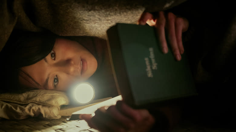 Dr. Ye Wenjie reading under a blanket with a flashlight in "3 Body Problem."