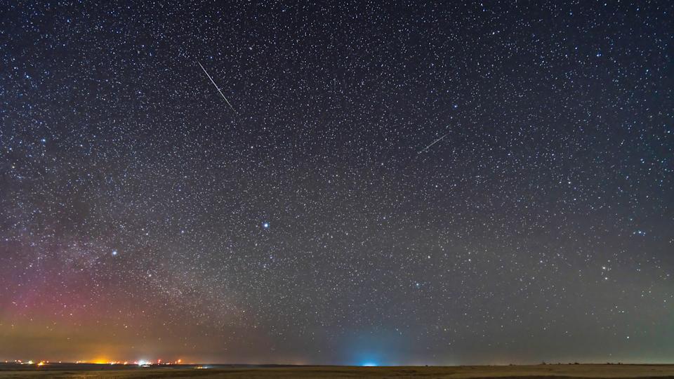 Two lone Lyrid meteors on the peak of the meteor shower night, April 22, 2023. The sky and ground come from the exposure with the bright meteor on it, when a dim aurora was also on the northeast horizon. The bright meteor shows the classic green to pink gradient of colours. Vega and Lyra are rising at lower centre. Deneb and Cygnus are at left. Arcturus is at upper right