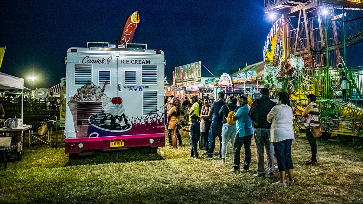 Customers line up alongside Carvel ice cream truck at New Jersey fair in the evening.