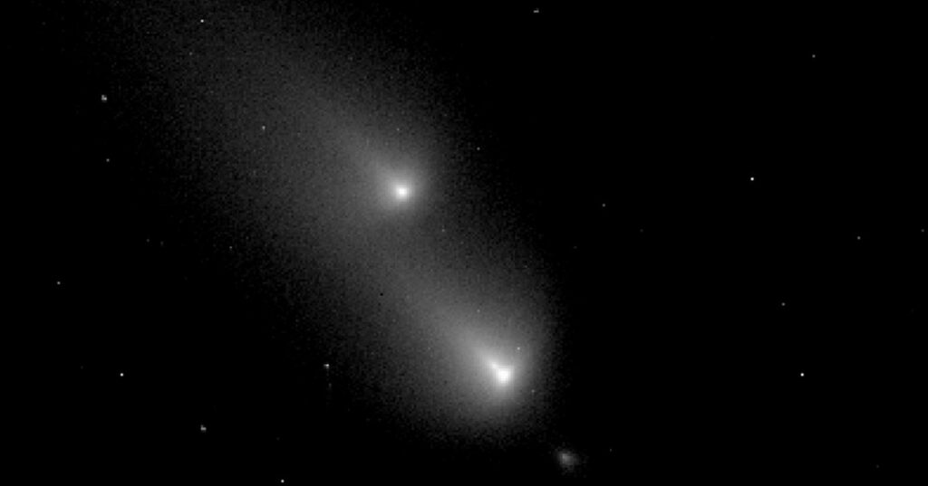 Hubble Space Telescope image of a comet breaking apart, showing multiple bright fragments surrounded by a hazy cloud of dust against a dark, star-filled background.