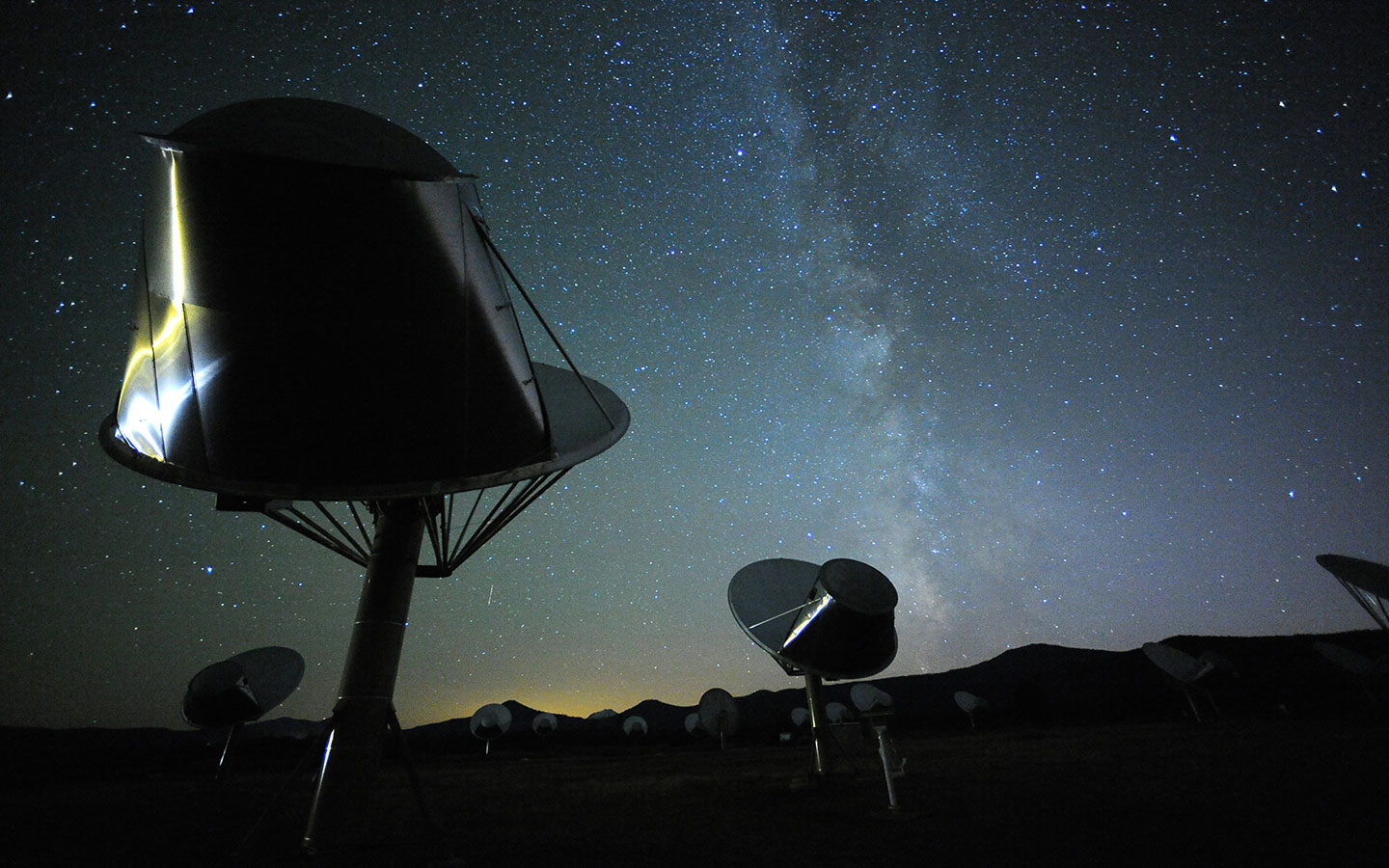 an array of round antenna dishes aim skyward amid a desert landscape