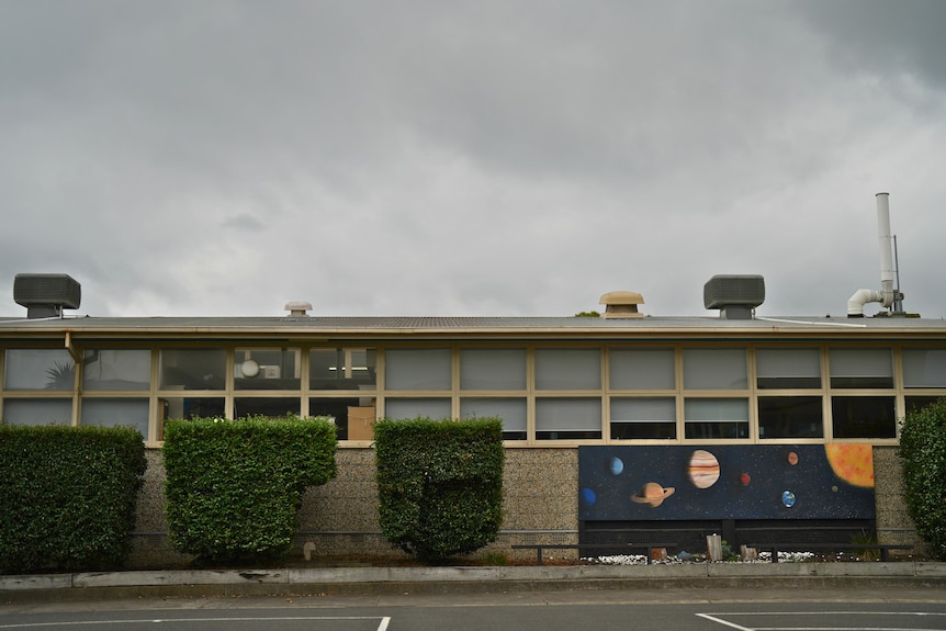 A single story brick education building in muted tones with a mural depicting planets outside