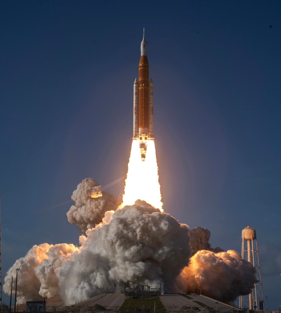 NASA's Artemis II Space Launch System rocket launching from Kennedy Space Center, emitting bright orange fire and thick white smoke.