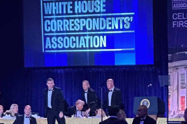 Secret Service agents surround Donald Trump, who is seated at a table on a stage