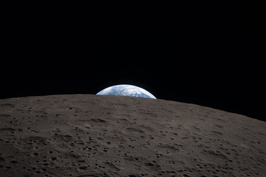 In this deep-space image from NASA's Artemis II mission, a sliver of Earth peeks over the limb of the moon, which dominates the foreground.