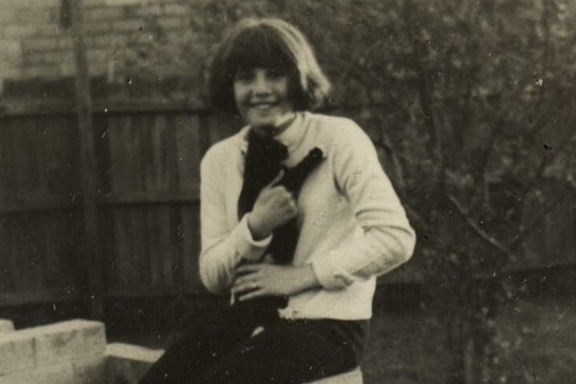 Black and white image a young girl with bob haircut sitting on brick structure in front yard holding a cat