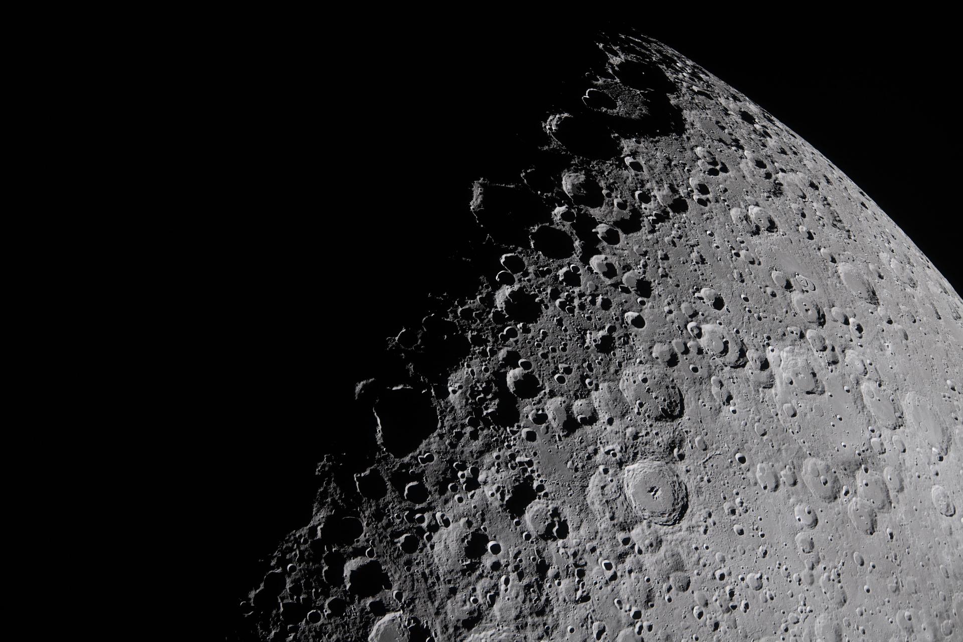 A close up of the moon's surface, its gray landscape dotted by small round craters. Its left half is in shadow.