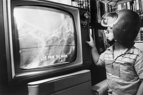 Black and white 1960s image little boy in helmet watching moon landing on vintage tv