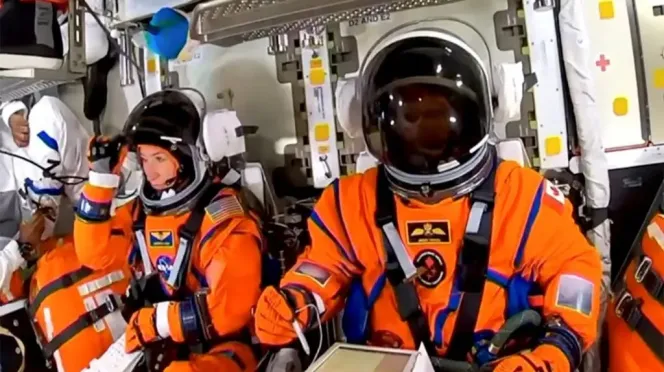 Astronauts in orange spacesuits with helmets on, preparing for the Artemis II mission.