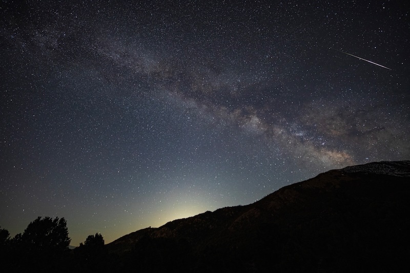Milky Way with a bright Lyrid meteor. Some trees and a hill are in the foreground.