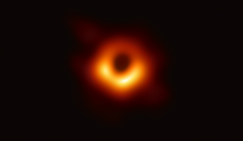 A bright, slightly irregular, fiery orange ring of light with a large, dark, circular central void, isolated against a solid black cosmic background
