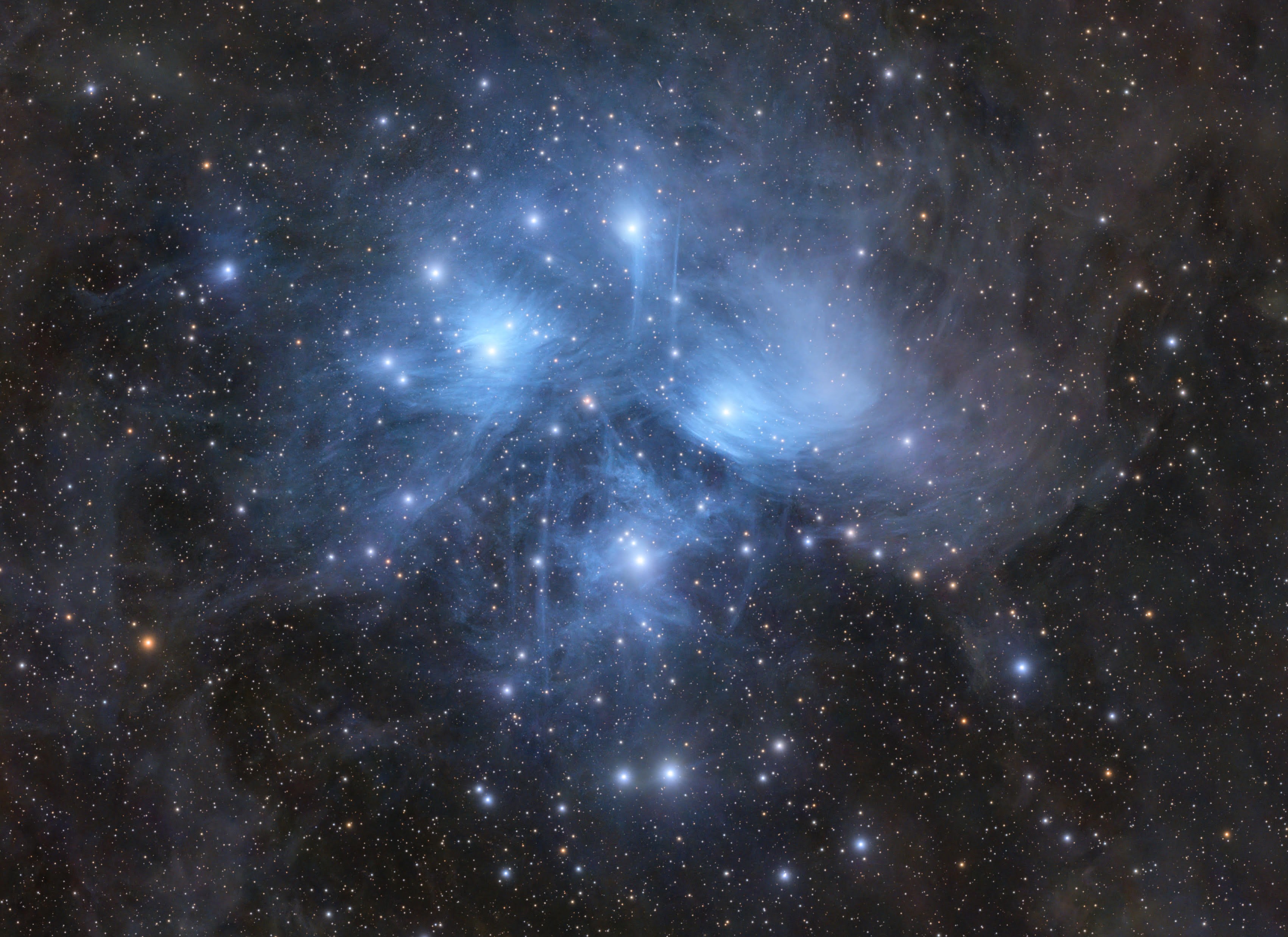 The stars of the Pleiades open cluster shine brightly against a more distant starfield, while surrounded by blue nebulosity.