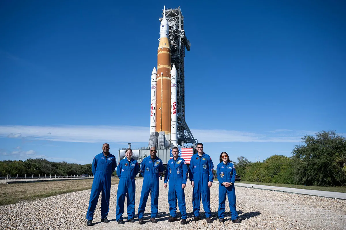 Six people in blue boiler suits stand in front of rocket.