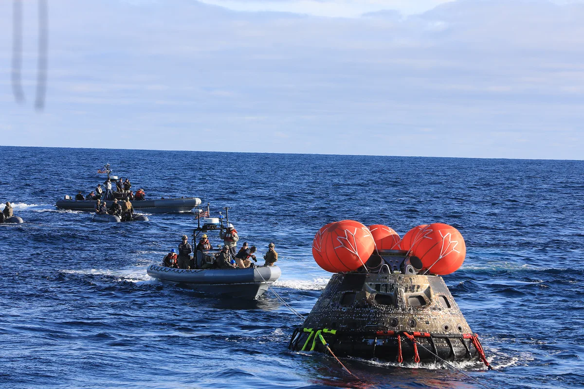 The Artemis I Orion capsule floating in the ocean with recovery boats
