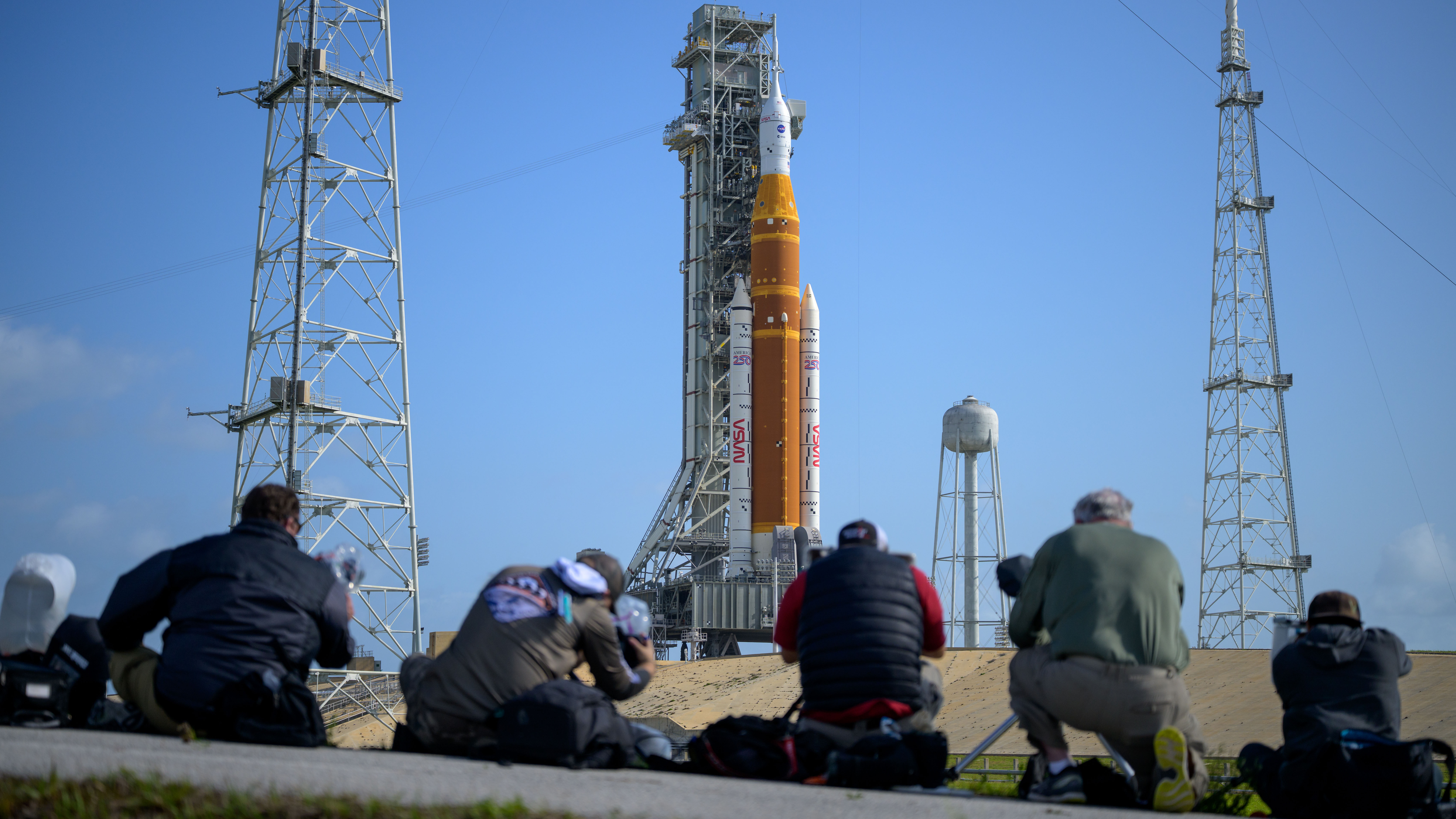 Media aim their remote cameras on NASA’s Artemis II Space Launch System (SLS) rocket and Orion spacecraft, atop a mobile launcher at Launch Complex 39B, Sunday, March 29, 2026, at NASA’s Kennedy Space Center in Florida. NASA’s Artemis II test flight will take Commander Reid Wiseman, Pilot Victor Glover, and Mission Specialist Christina Koch from NASA, and Mission Specialist Jeremy Hansen from the CSA (Canadian Space Agency), around the Moon and back to Earth with launch opportunities beginning in April 2026. Photo Credit: (NASA/Bill Ingalls)
