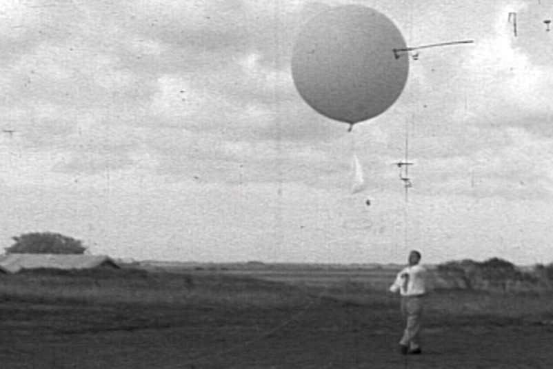 Black and white image man next to a weather balloon in sky