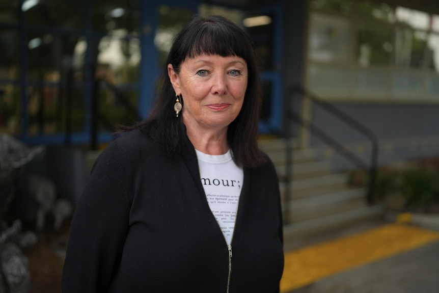 A woman with long dark hair and a fringe stands outside a building