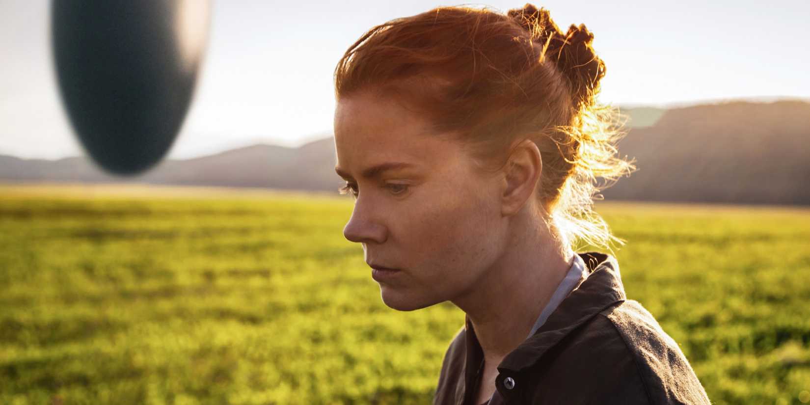 Arrival - 2016 - Amy Adams stands thinking in a field, a spacecraft in the distance behind her