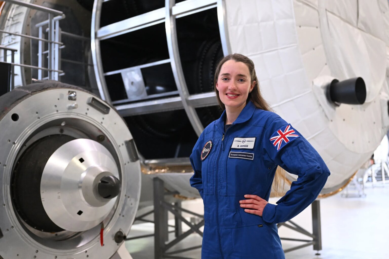 The British astronauts hoping to book a seat on the next moon missions Rosemary Coogan, an ESA astronaut candidate, poses in a blue flight suit with a British flag patch on her arm, in front of a spacecraft module.