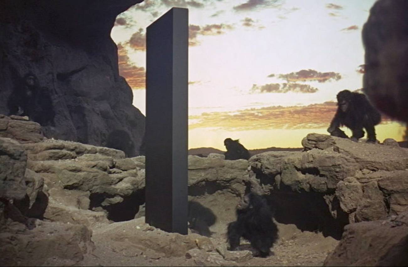 A group of early ape-like hominids gathered around a black monolith in 2001: A Space Odyssey