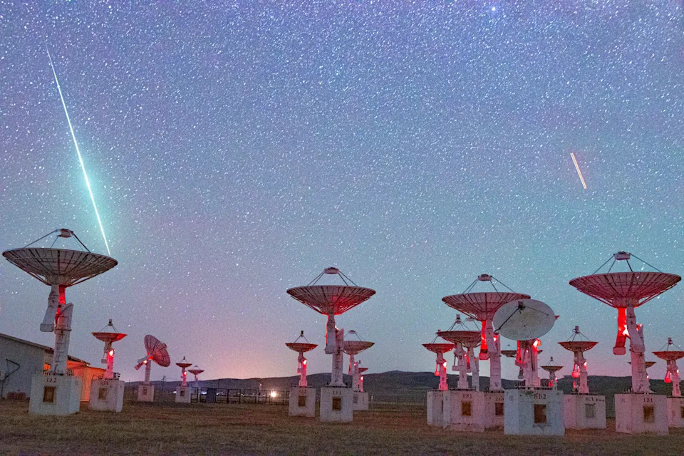 Shooting stars in a night sky above an array of parabolic antennas.