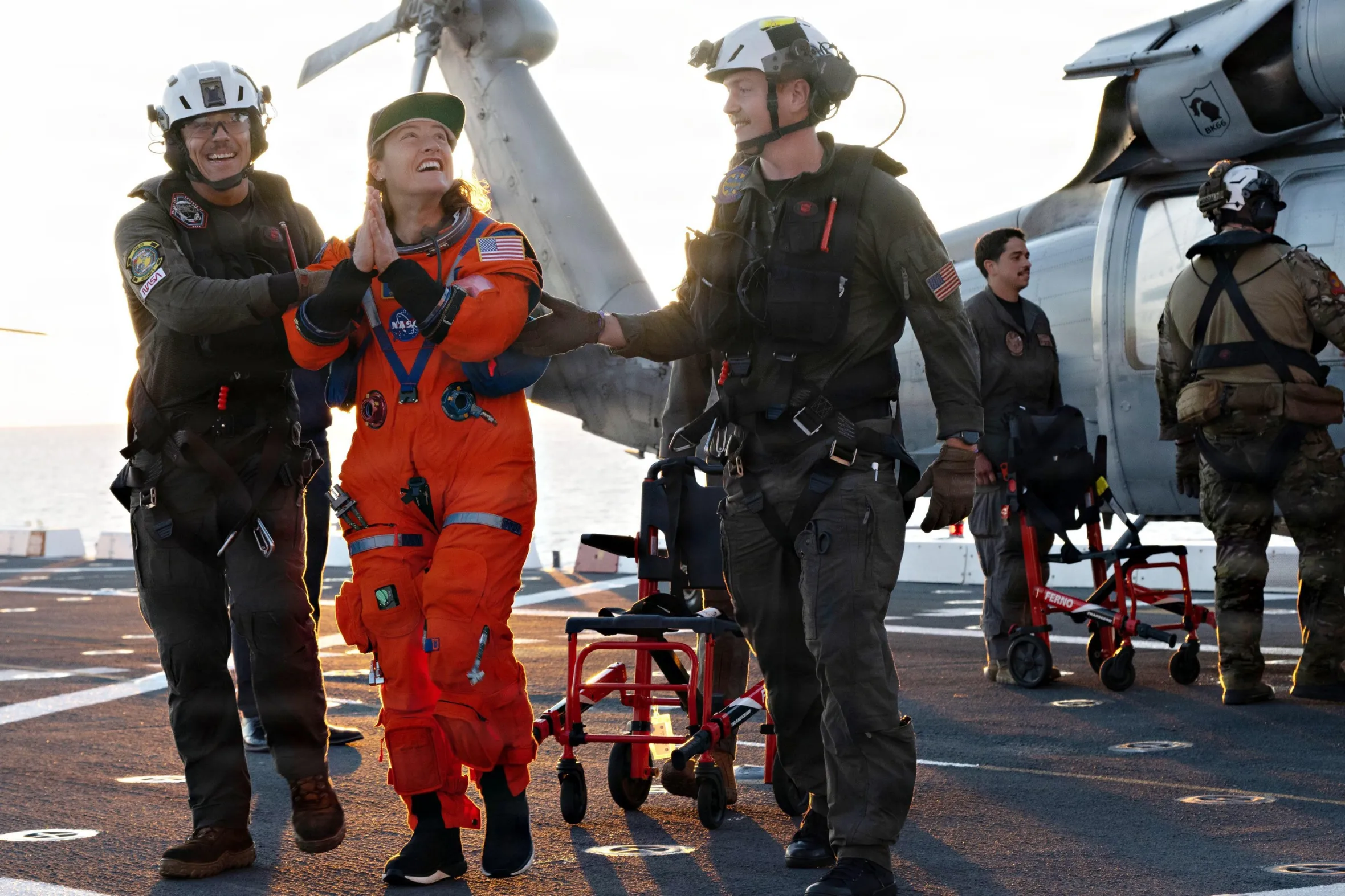Astronaut Christina Koch is assisted off the flight deck of the USS John P. Murtha by crewmates.
