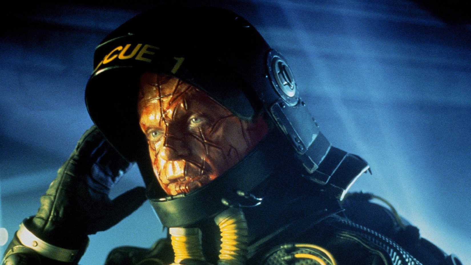 Sam Neill lifts the visor of his space suit to reveal a scarred face in Event Horizon