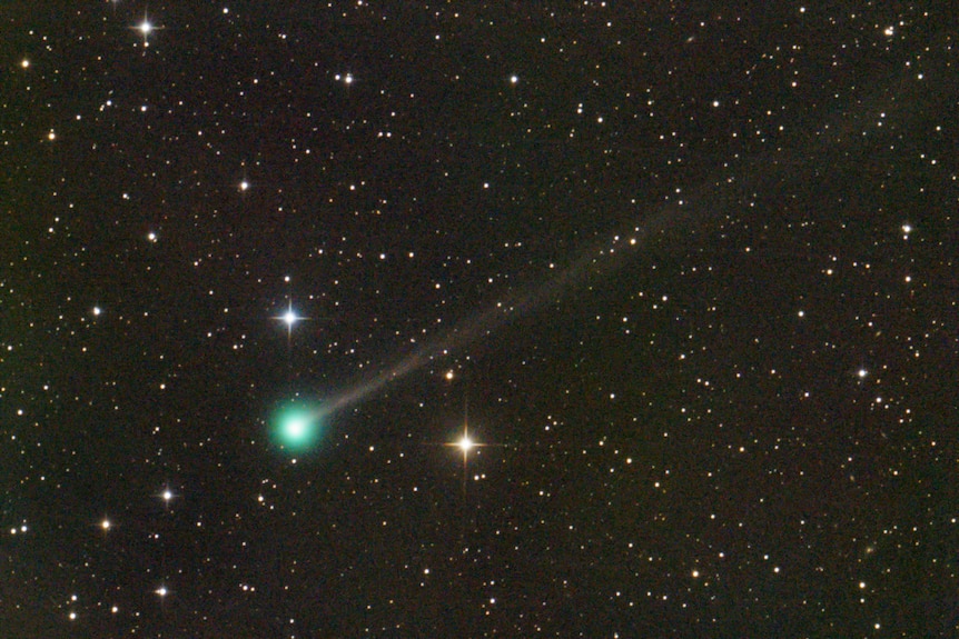 Starfield with bright comet in the centre, with a bright green head and a more faded tail.