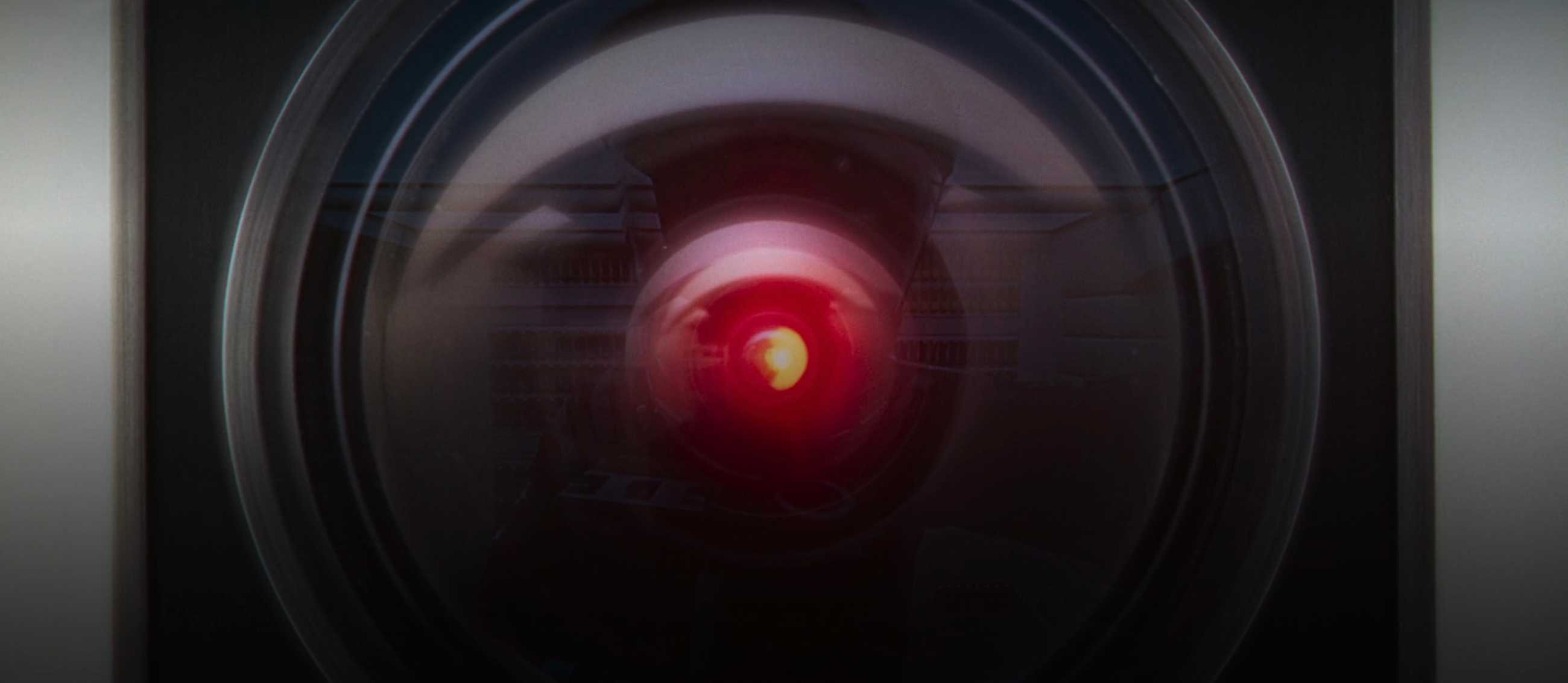 A closeup of the red lens eye of HAL 9000, with a human figure in a spacesuit reflected in it, in 2001: A Space Odyssey