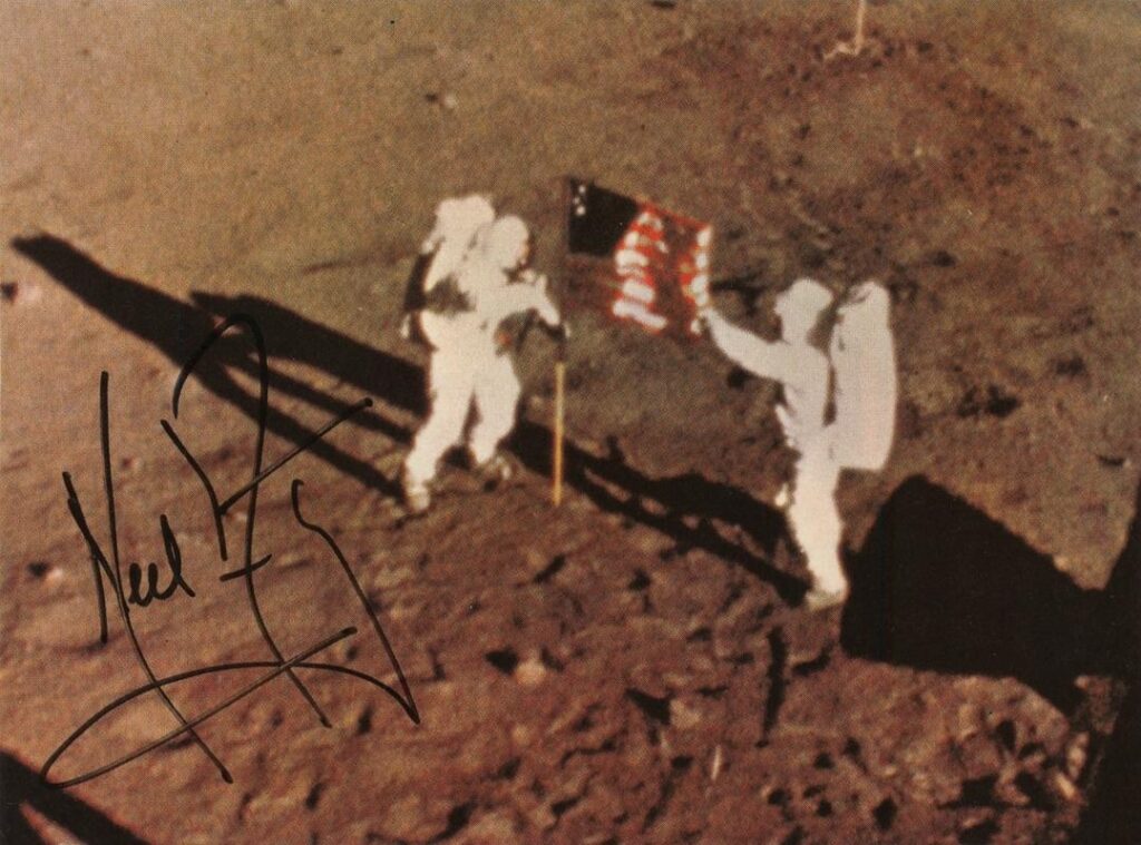 Rare color 4.25 x 3.5 cardstock photo showing the Apollo 11 astronauts after planting the American flag on the lunar surface, signed in black felt tip by Neil Armstrong.
