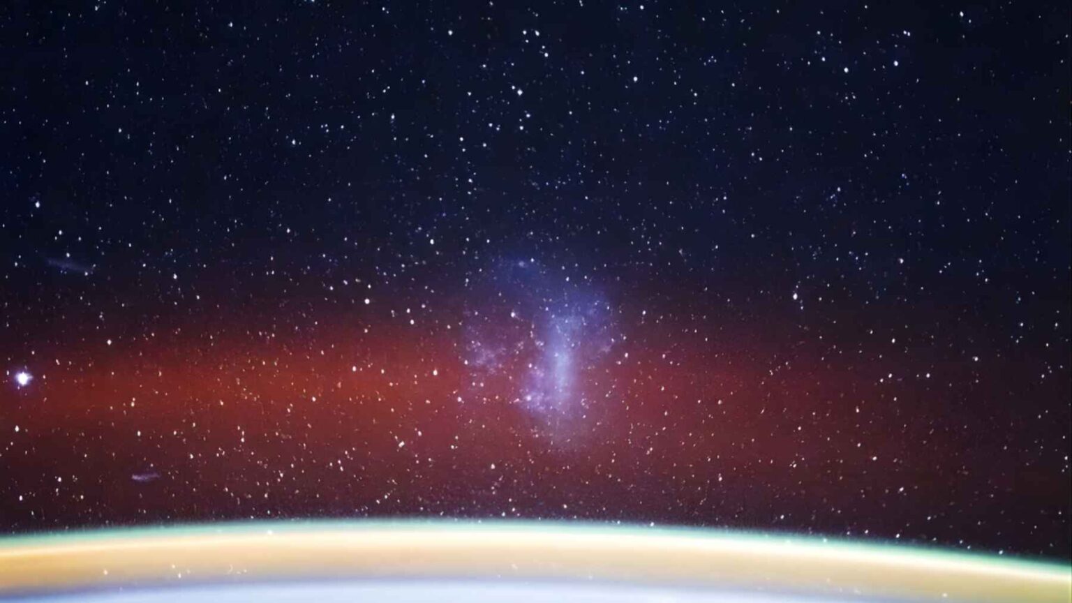 View from the International Space Station showing Earth’s glowing horizon and the Large Magellanic Cloud as a bright patch in a star-filled sky.
