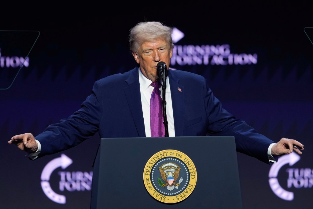 Donald Trump speaking at a Turning Point USA event from a podium with the Seal of the President of the United States.