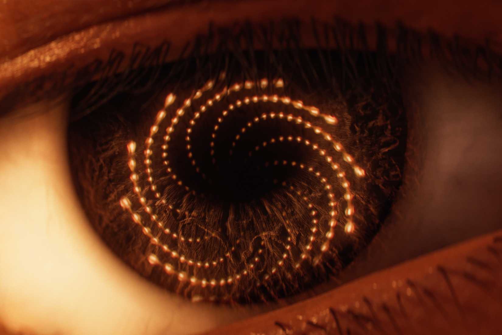 Close-up of an eye with glowing spiral patterns reflecting cosmic imagery