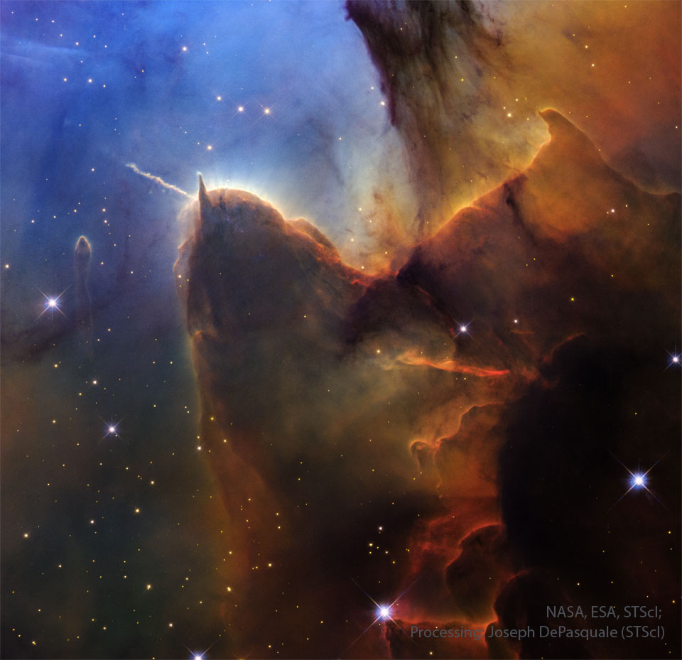 A field of stars on the left is mirred by a wall of
opaque brown dust on the right. Jutting out from the wall is
a long pillar with a rounded end that has a prominent light-
colored jet emanating toward the upper left. The stellar 
background toward the upper left is dark blue.
Please see the explanation for more detailed information.