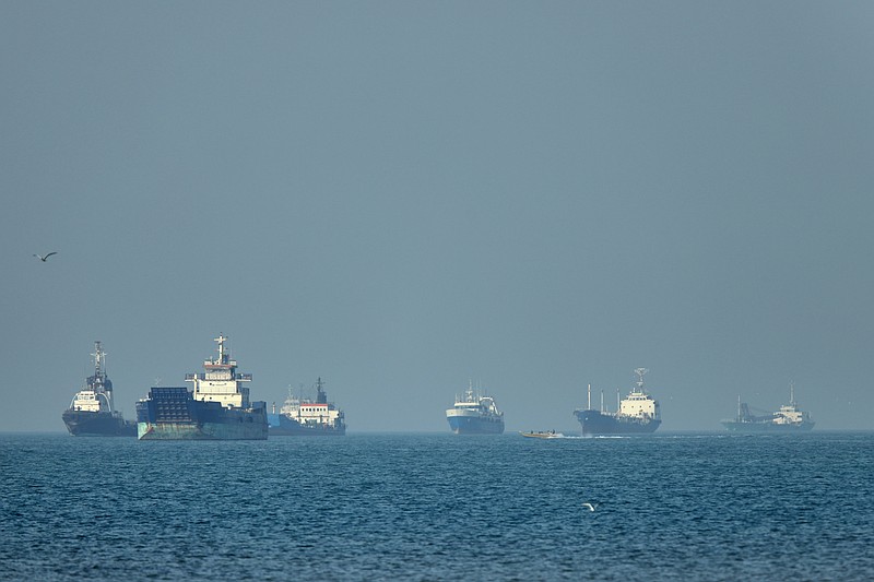 Cargo ships, including bulk carriers and general cargo vessels, sit at anchor offshore as a small motorboat passes in the foreground, in the Strait of Hormuz off Bandar Abbas, Iran, Monday, May 4 , 2026.(Amirhosein Khorgooi/ISNA via AP)