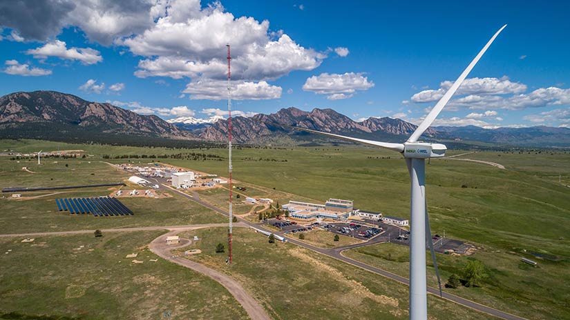 Composites Manufacturing Education and Technology Facility | Wind Research A wind turbine stands in the foreground with roads and buildings below. A mountain range spans the background.