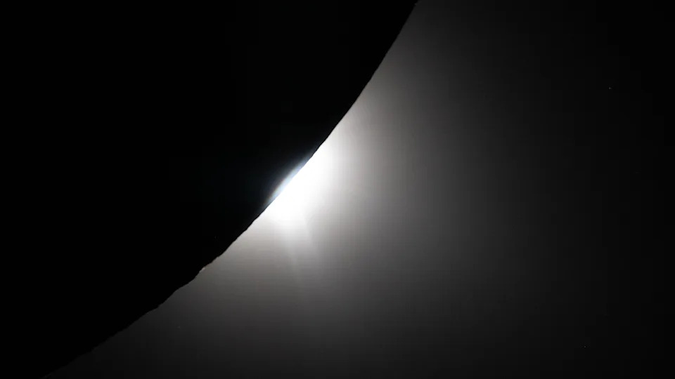 A silhouette of the curve of the bottom half of the moon, with glowing white light behind it. 