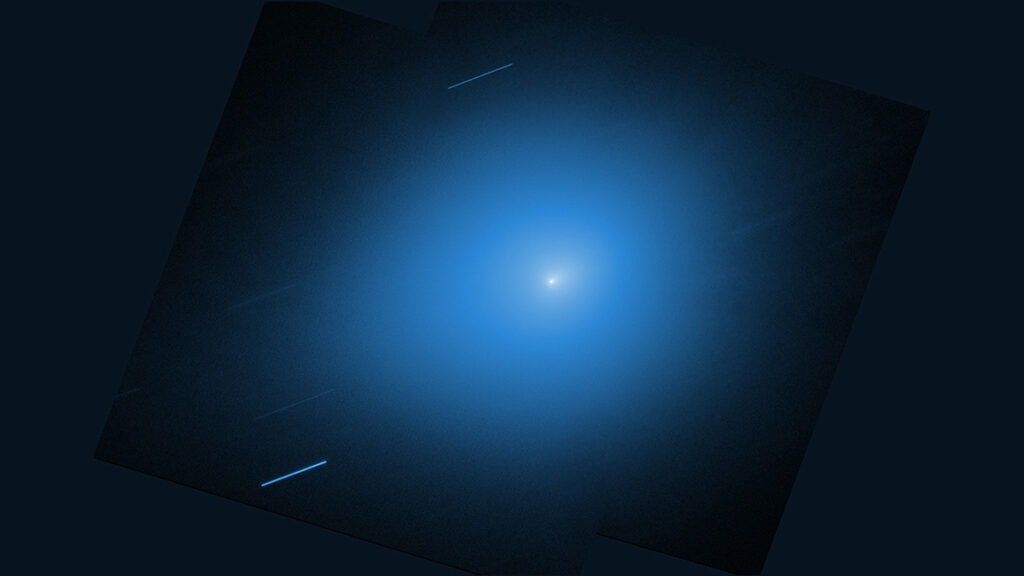A bright white point is surrounded by a large, soft blue glow that fades gradually into a dark background. Thin, faint streaks appear diagonally across the image, suggesting motion or stars in the distance. The overall effect is of a luminous object in space, radiating light against a deep, dark backdrop.