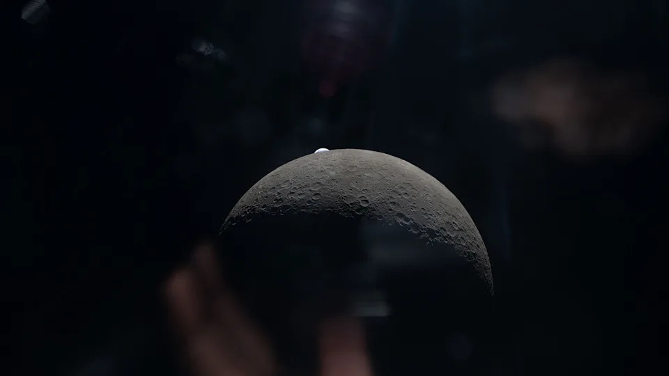 A view of the gray sphere of the moon in space, with a faint blue Earth behind it. 