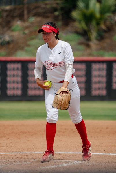 Palomar softball pitcher in a white uniform holds a yellow softball and prepares to pitch.