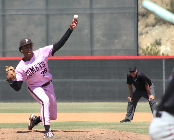 A left-handed Palomar baseball pitcher in a pink uniform strides toward the mound as he is about to release a pitch.