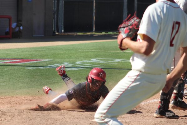 Palomar baseball player in dark grey sprays up dirt as he slides into home plate.